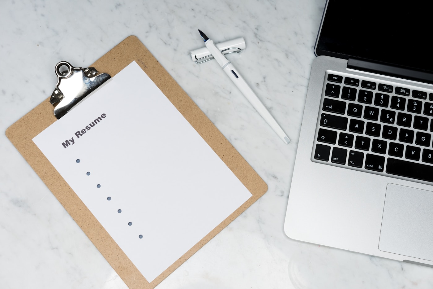 An open notebook beside a small digital recorder on a wooden desk with proof sheets.